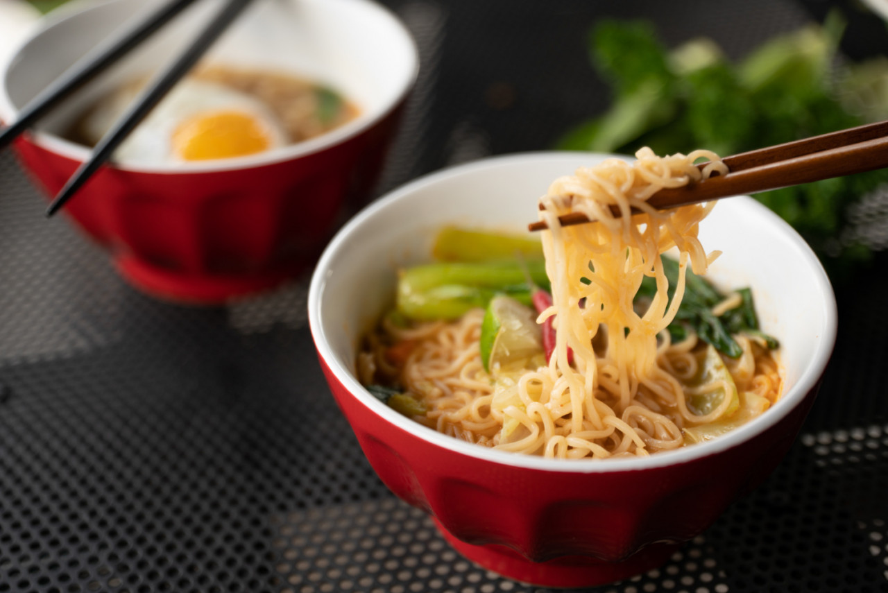 close shot chopsticks with noodles near soup with blurred background