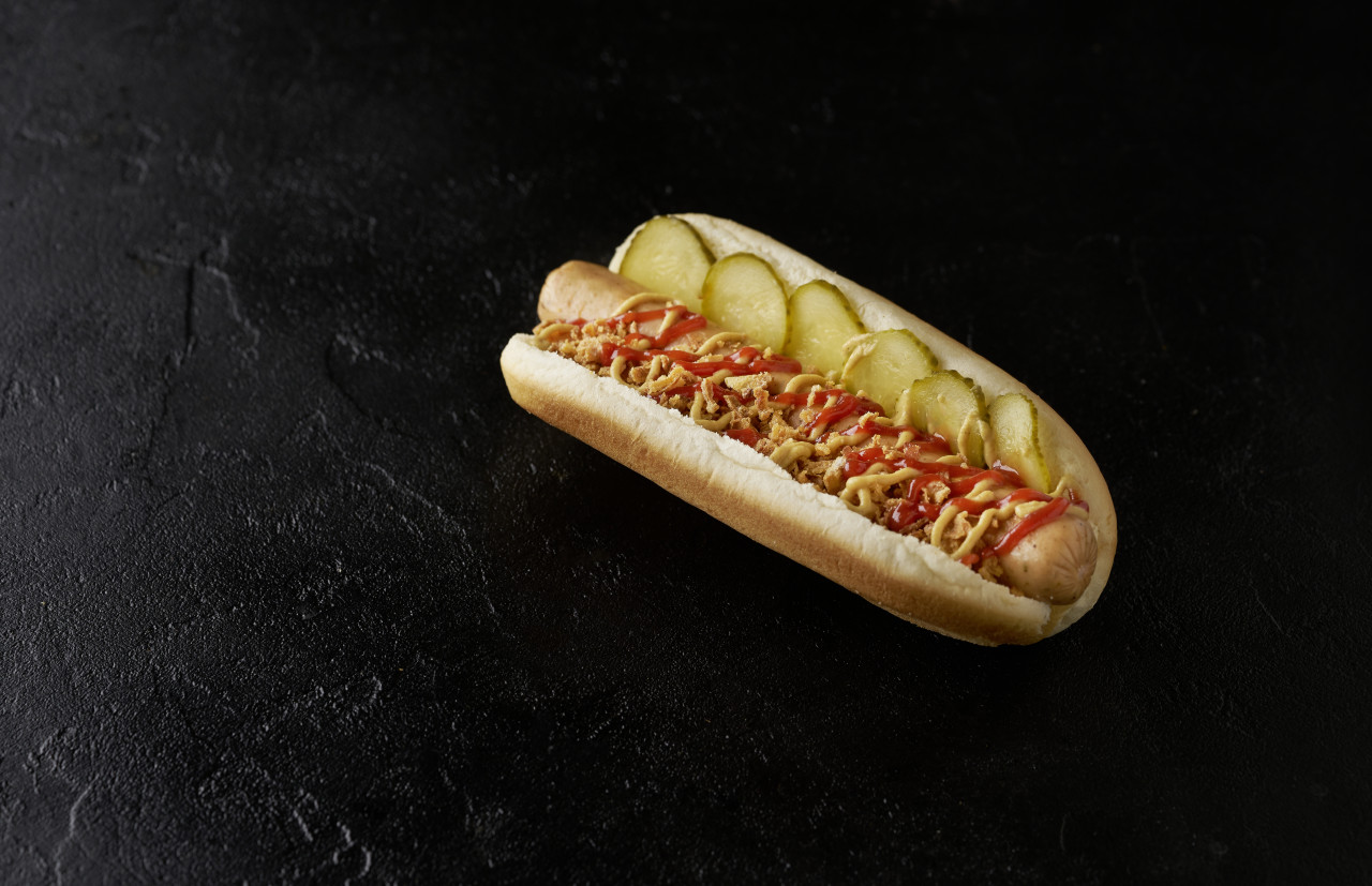 hot dog with pickled cucumbers fried onions ketchup mustard black background