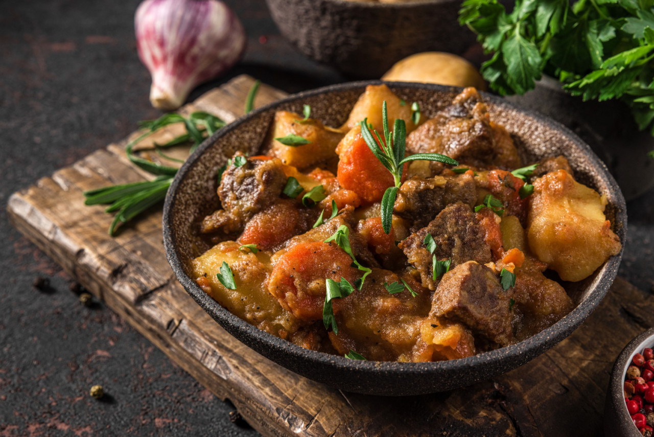 irish stew made with beef meat potatoes carrots herbs plate black surface