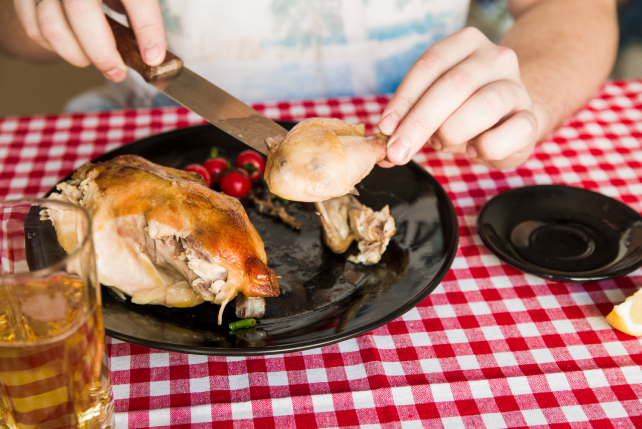 person s hand eating grilled chicken using knife while having dinner with glass beer table