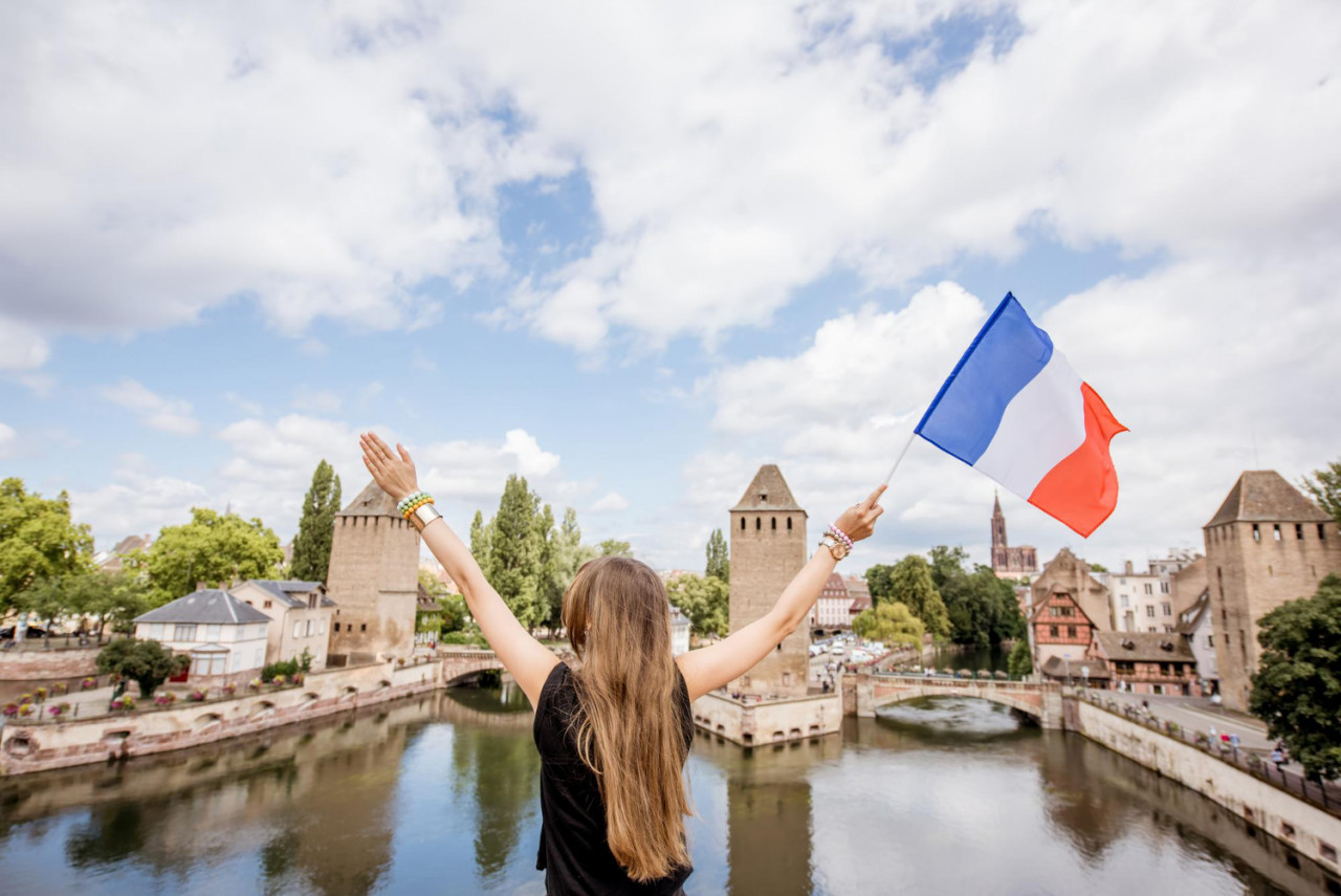 young woman tourist sitting back with french flag beautiful landscape background with river towers old town strassbourg city france