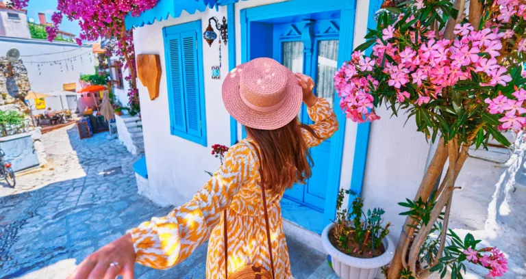 Follow Me Concept Girl Traveler Wearing Dress Hat Walks Beautiful Colorful Flower Street With White Houses Blue Doors European City