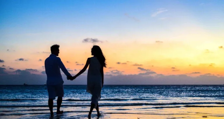 Man And Woman Holding Hands Walking On Seashore During Sunrise