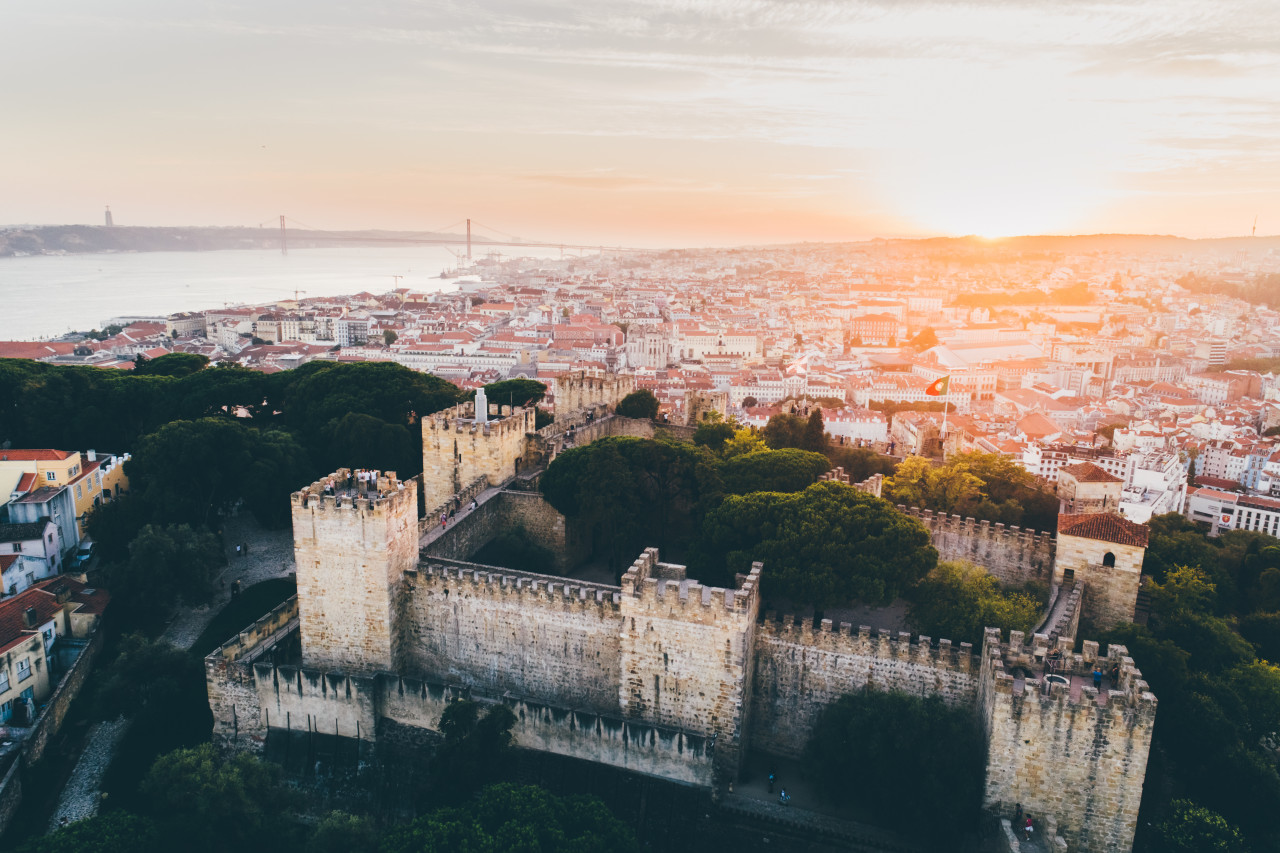 aerial view medieval fortress hill top lisbon drone flying ancient wall castelo de sao jorge with flapping flags walking people sunset 1