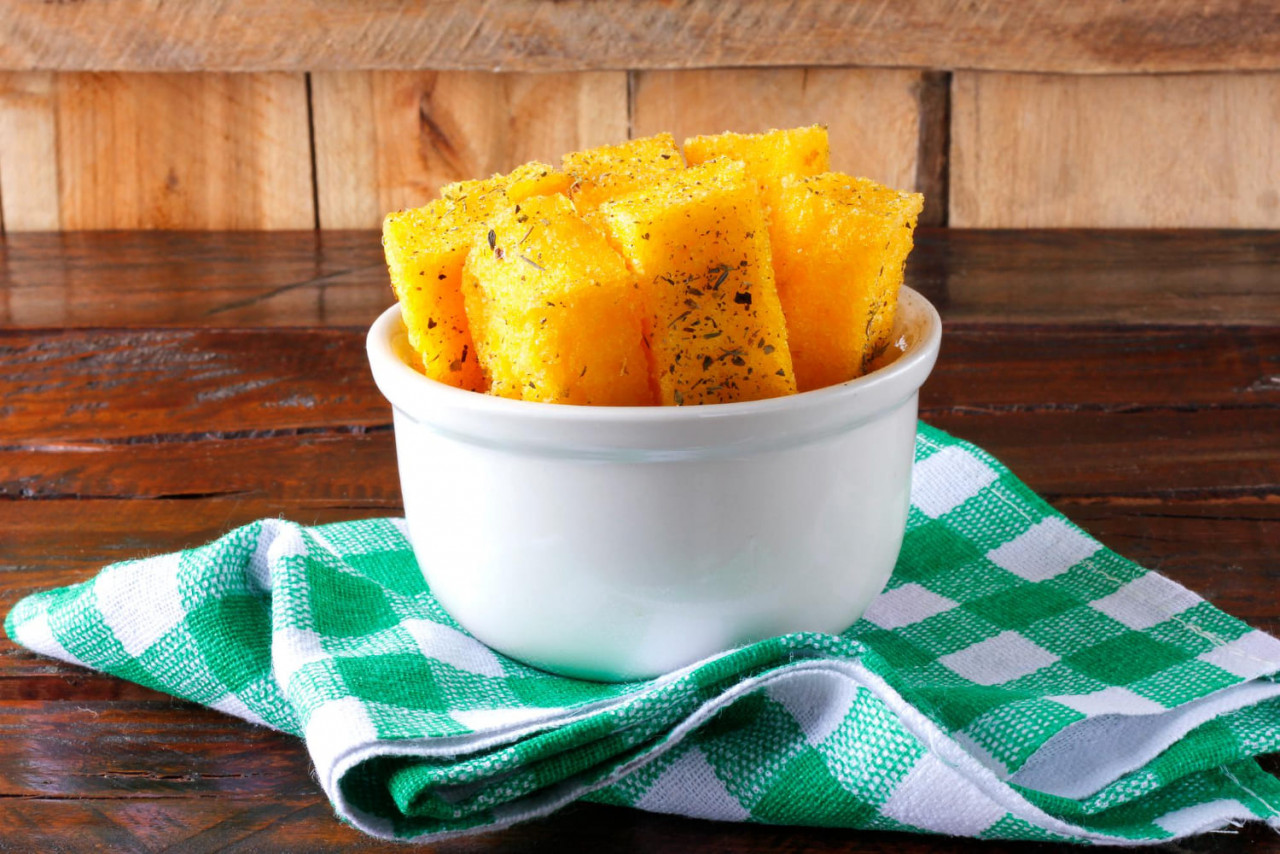 bastoncini di polenta fritti in ciotola di ceramica bianca su tavola di legno rustica