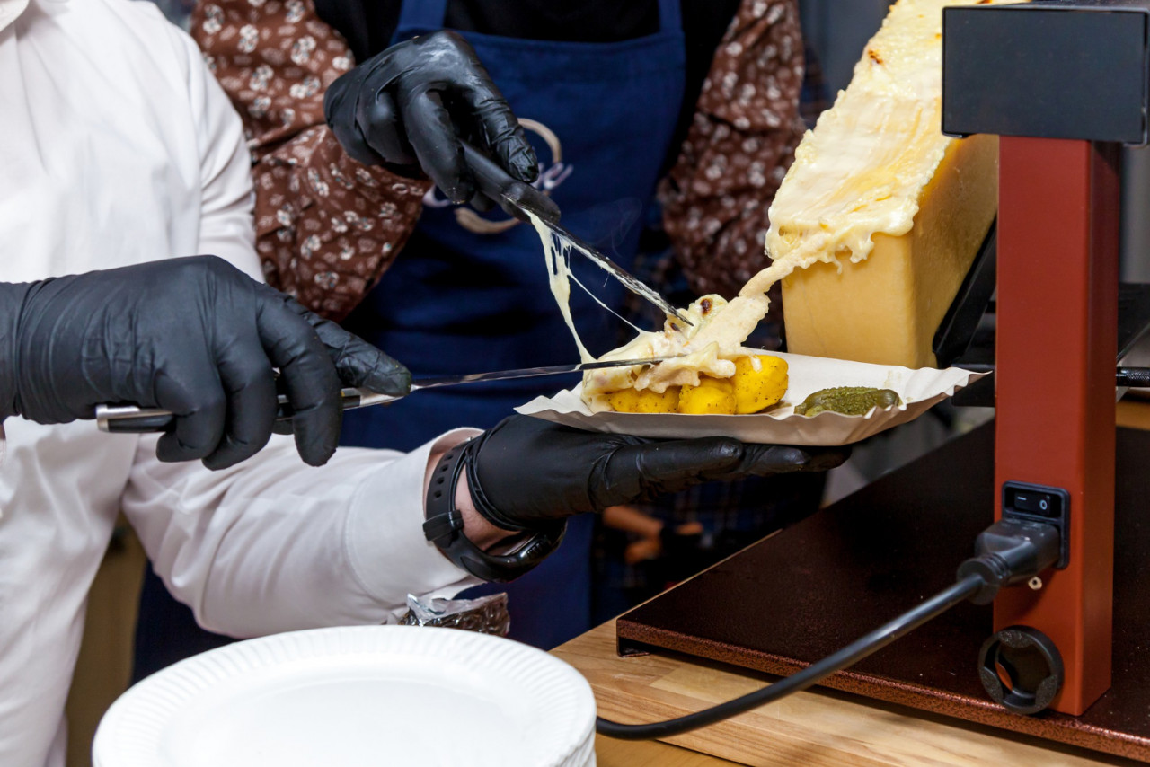 chef is preparing dish with raclette using special instrument cheese melting