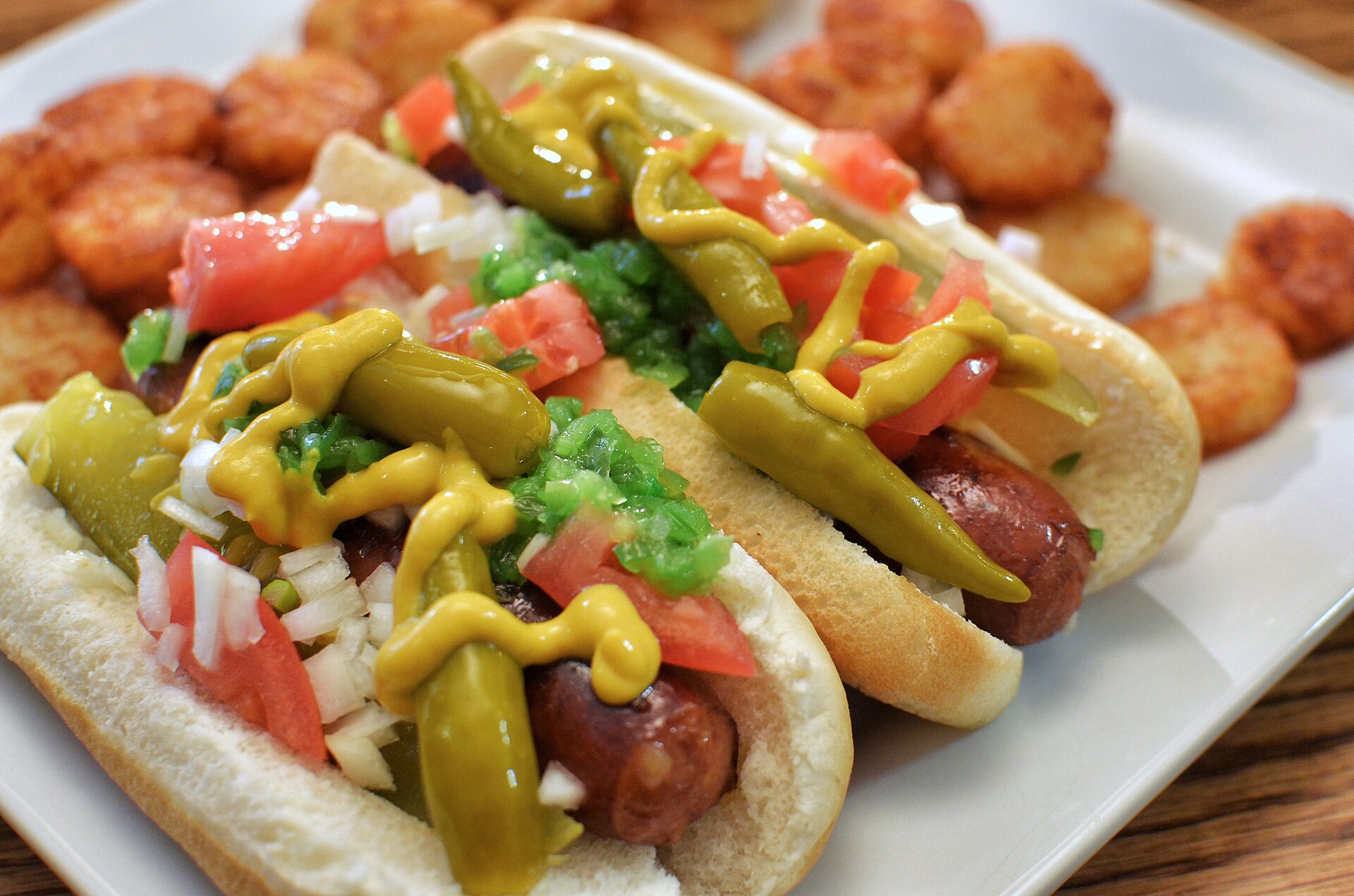 Un hot dog interamente guarnito con senape, cipolle bianche, relish verde brillante, pomodori, peperoncini sport peppers e un pizzico di sale di sedano.