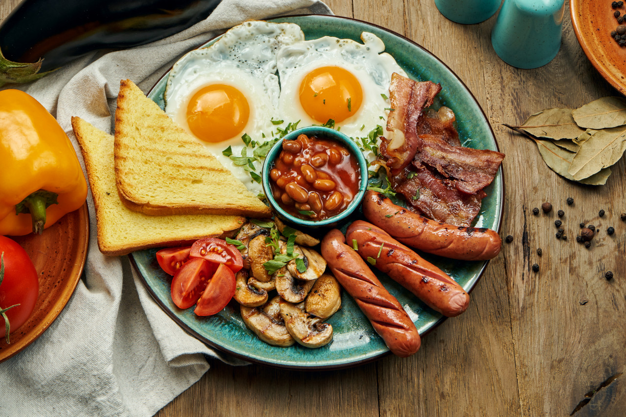 classic english breakfast toasts smoked sausages bacon fried eggs beans fried toasts blue plate top view horizontal wooden surface