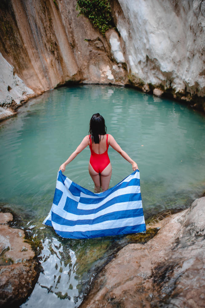 donna in costume da bagno rosso con bandiera greca cascata dimosari al famoso punto di riferimento dell isola di lefkada