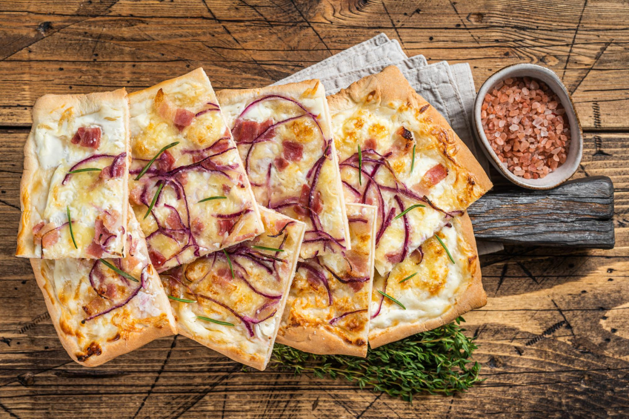 flammkuchen or tarte flambee with cream cheese bacon and onions wooden background top view