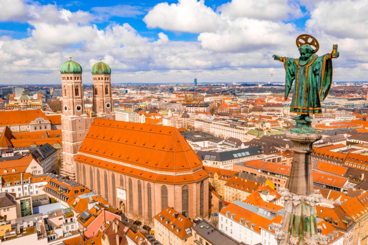 frauenkirche surrounded by buildings sunlight cloudy sky munich germany