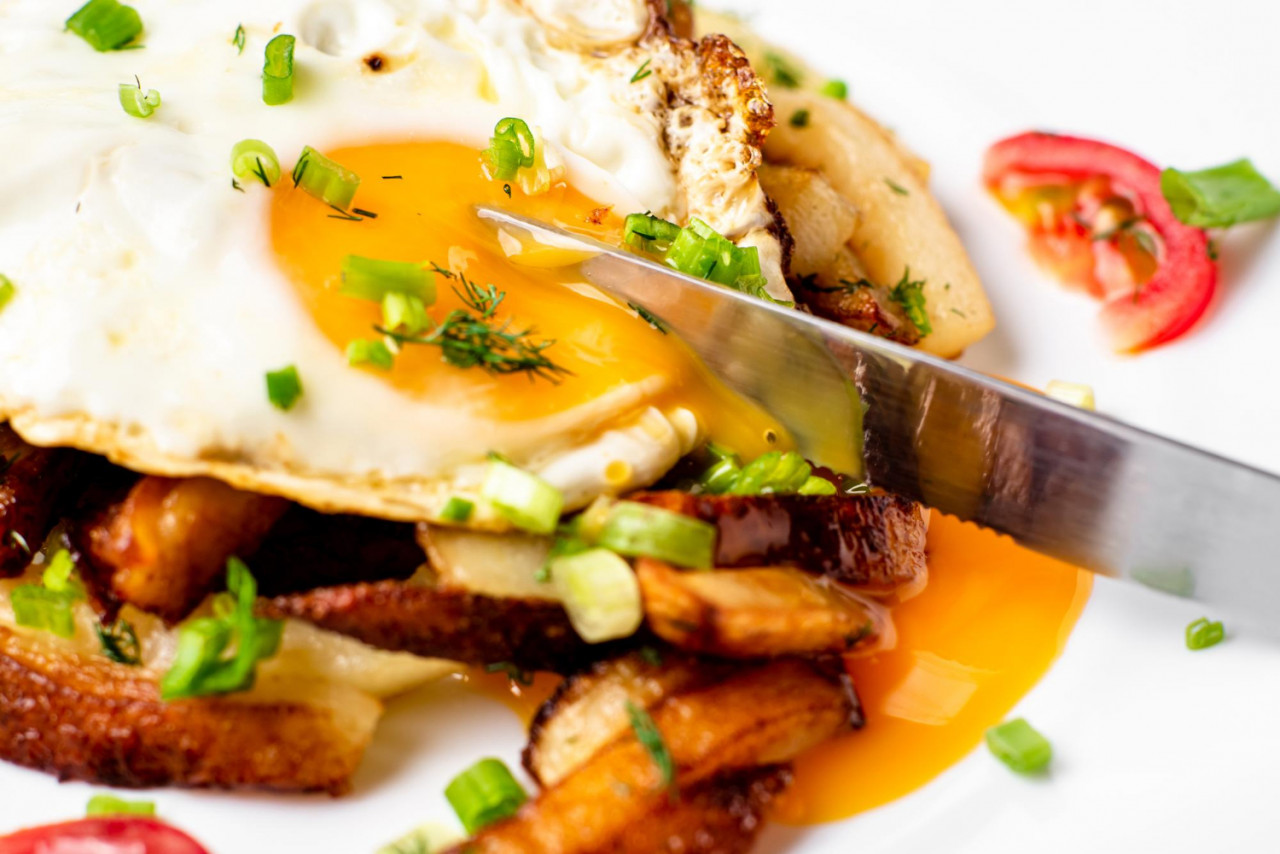 fried potatoes with egg with liquid flowing yolk herbs tomatoes white plate