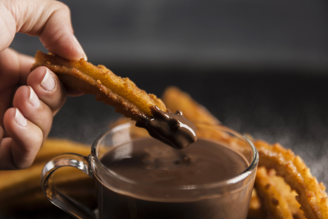 hand dipping fried churros chocolate