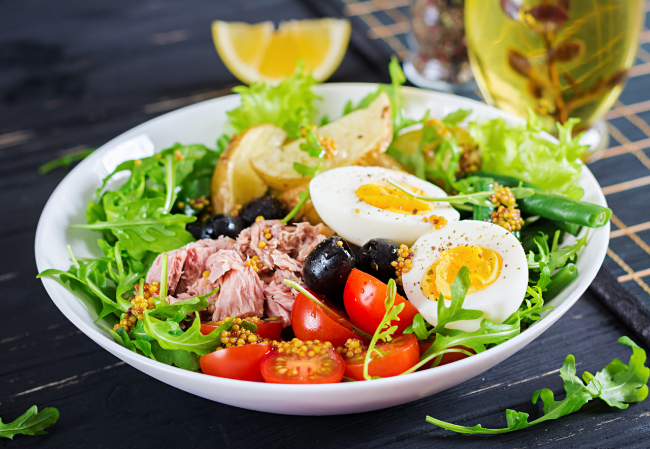 healthy hearty salad tuna green beans tomatoes eggs potatoes black olives close up bowl table