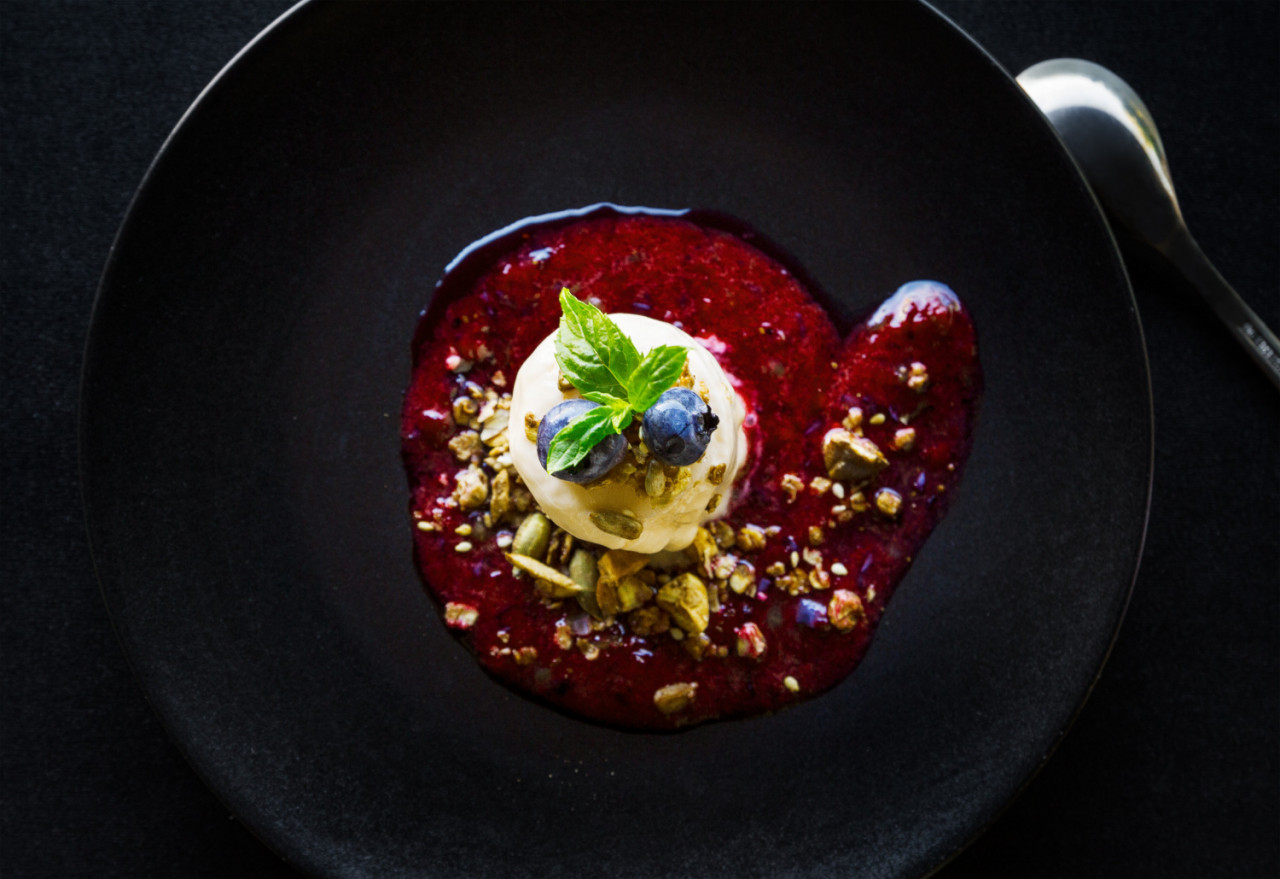 high angle shot of a delicious red dessert with white cream berries and nuts in a black bowl