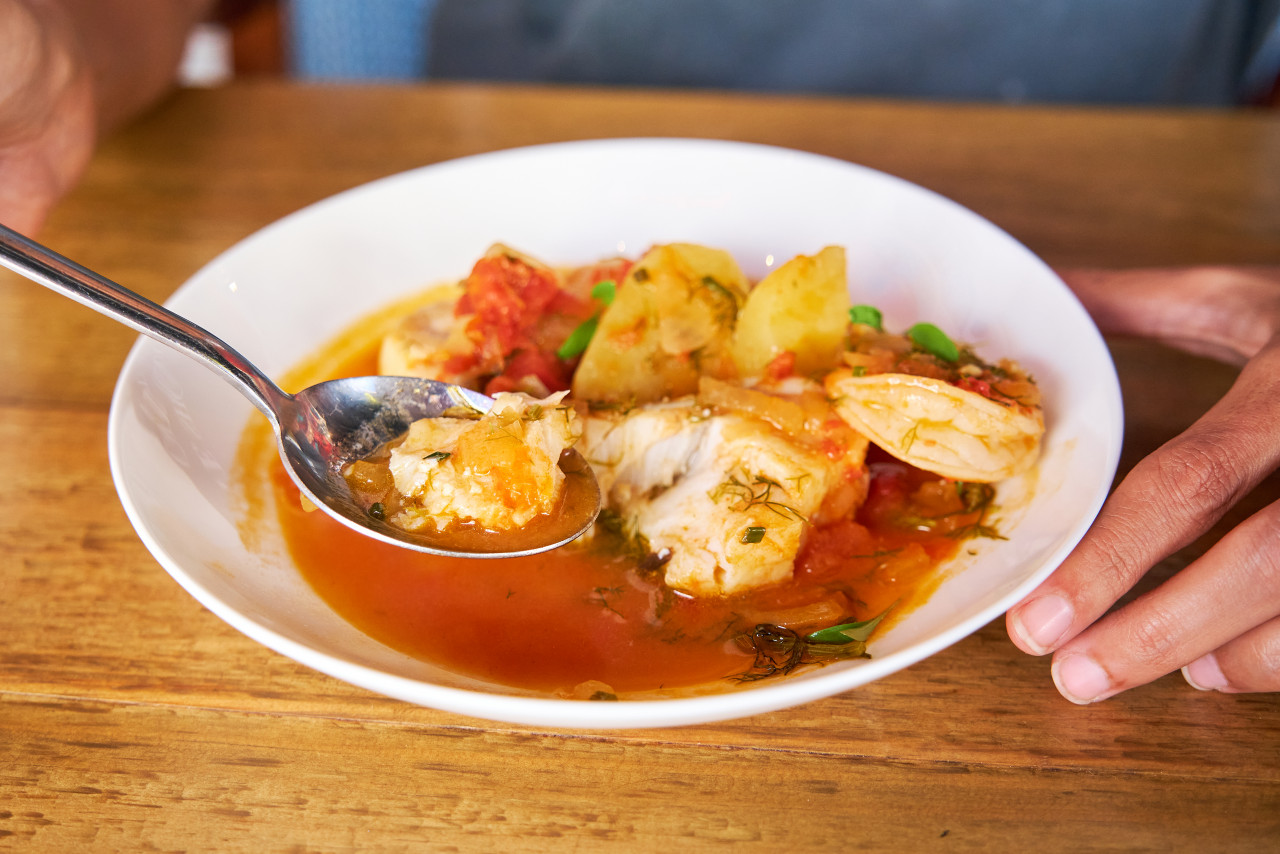 man eating with spoon from casserole with cod prawn with potatoes palm pepper aioli wooden table