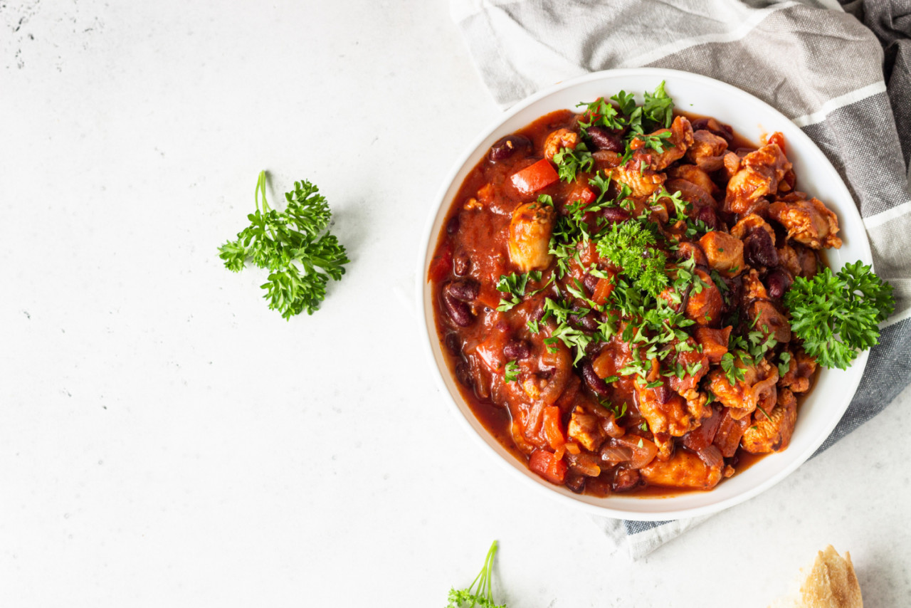 meat stew with red beans bell pepper onion tomato sauce white plate light grey slate