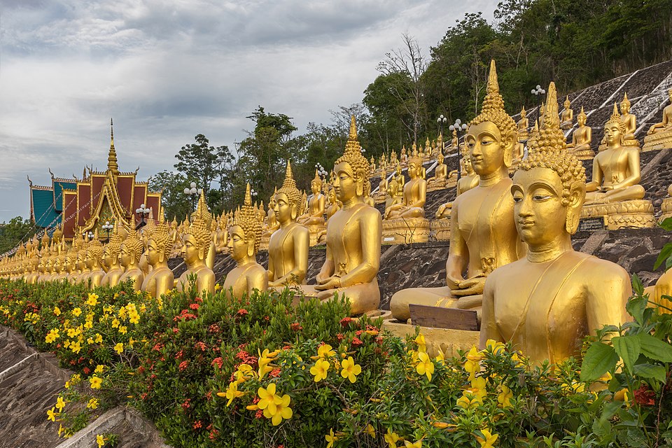 multiple rows of golden statues of the buddha seated with flowers at wat phou salao pakse laos