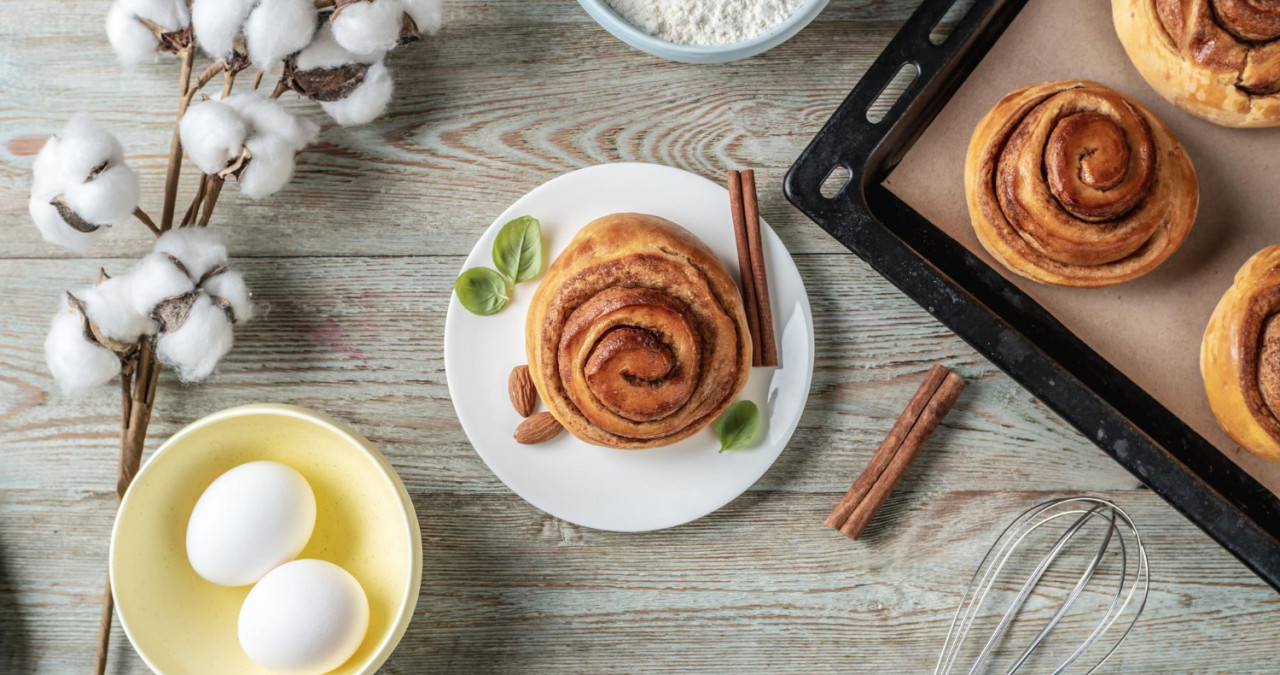 on the table is a baking tray with fresh cinnamon rolls ingredients for their cooking and an appetizing bun on a plate concept of tasty homemade pastries and a cozy atmosphere top view