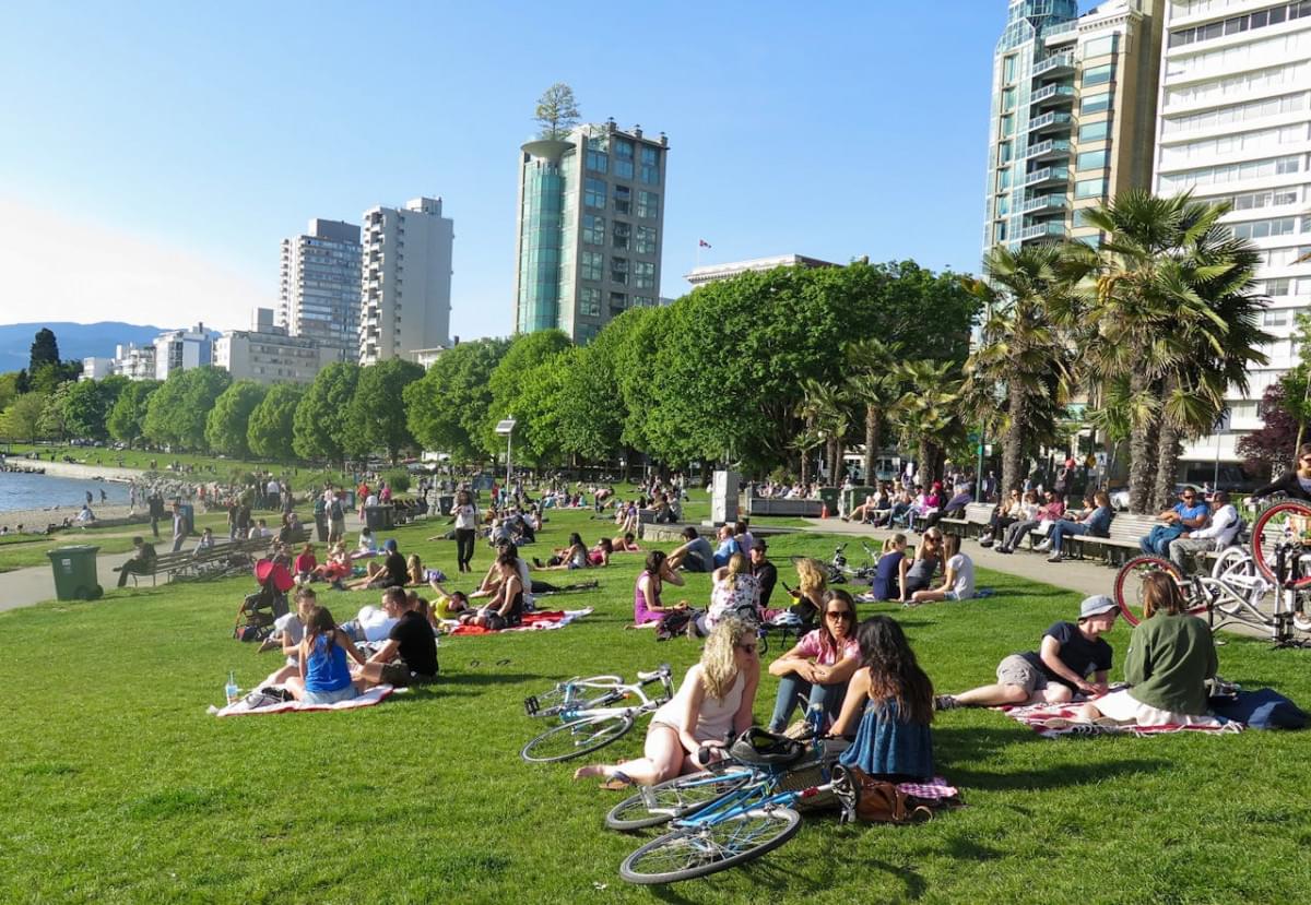 people sitting in a park in english bay vancouver canada