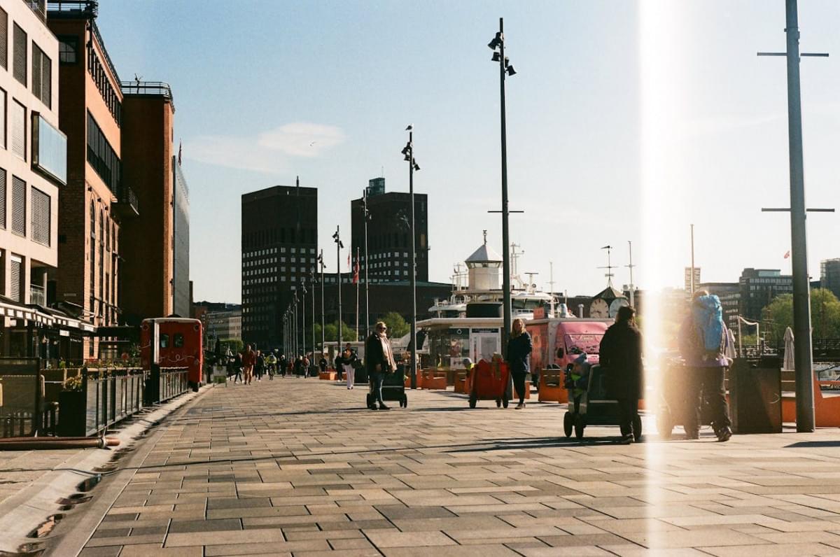 people walking on pier along fjord shore with oslo city hall in bac