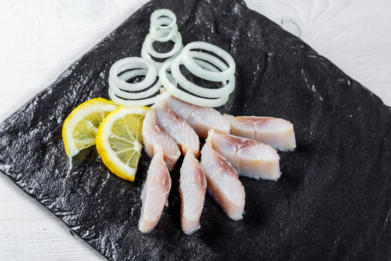 pieces salted herring with onion rings lemon slices black stone tray