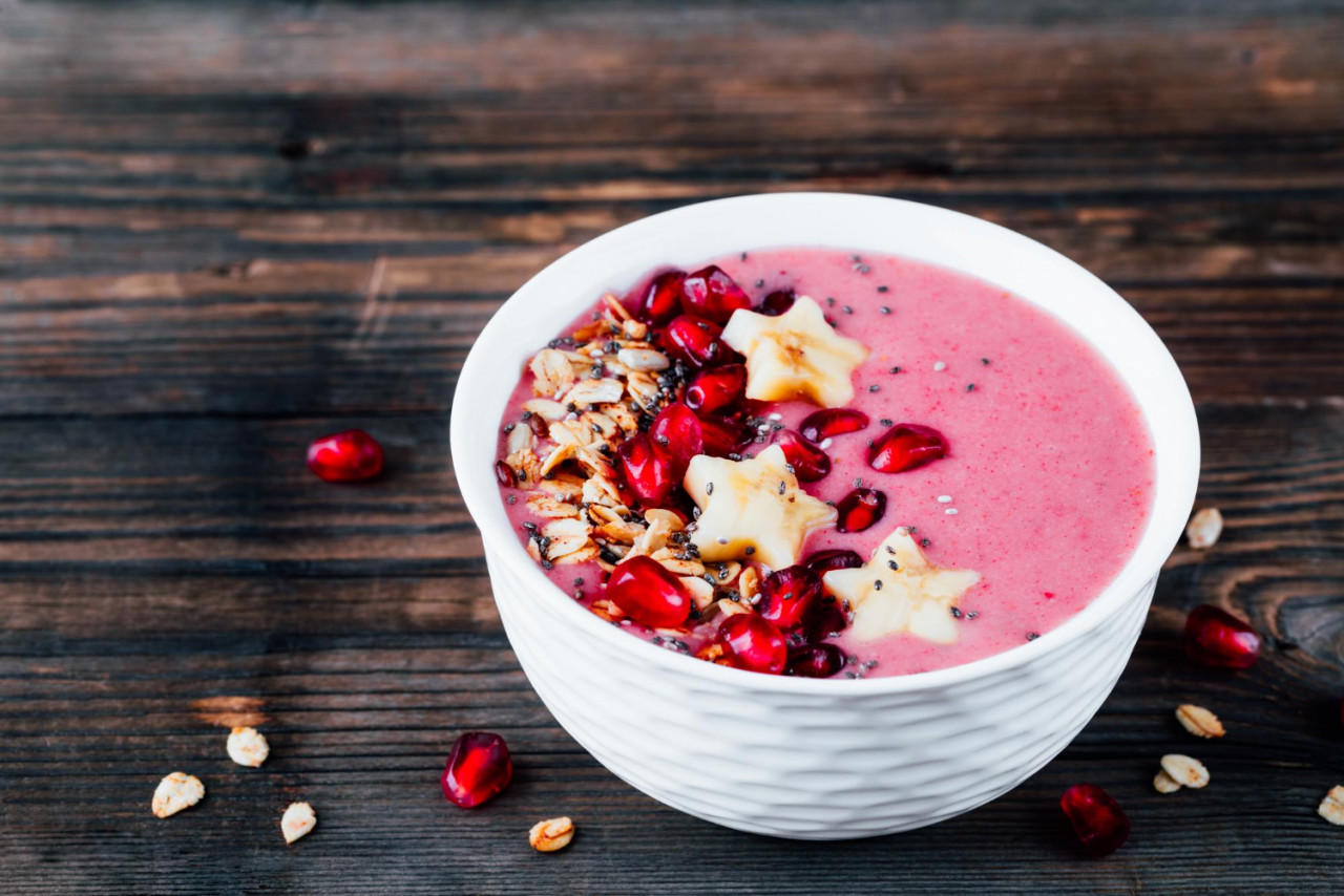 pink smoothie bowl with pomegranate homemade granola banana stars chia seeds wooden background