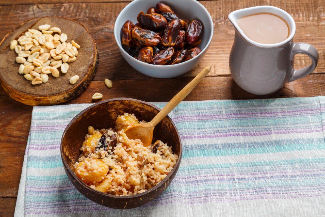 plate couscous wooden table with wooden spoon dates nuts jug fruit broth save place