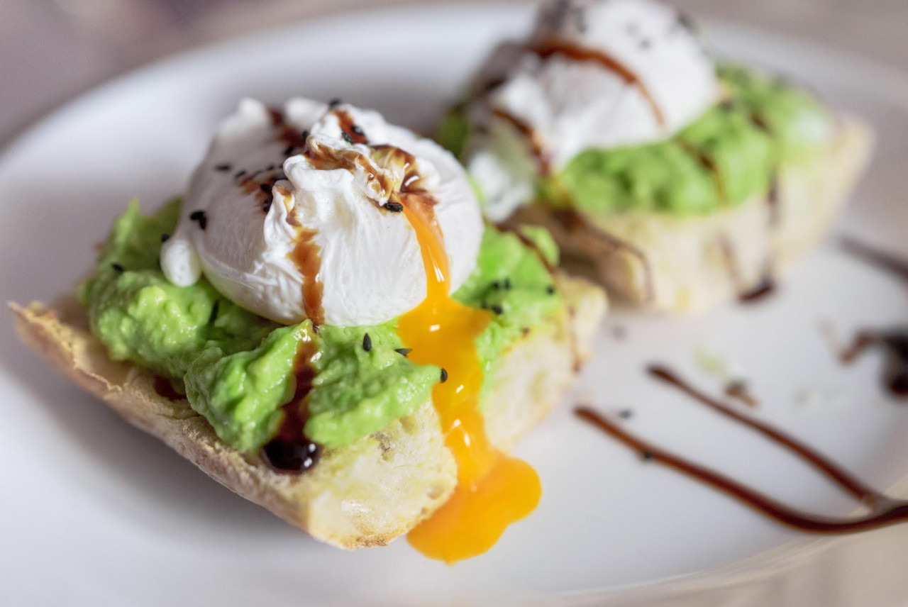 poached egg slice toast bread with guacamole dripping yolk white plate