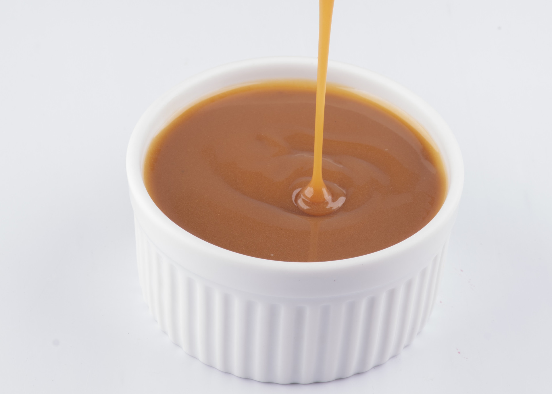 pouring dulce de leche with spoon into white pot isolated white backgr