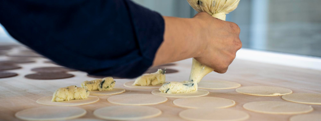 horizontal banner header with woman prepare fresh made ravioli inside pasta factory using pastry bag sac poche make stuffed pasta ravioli culurgiones agnolotti focus stuffed