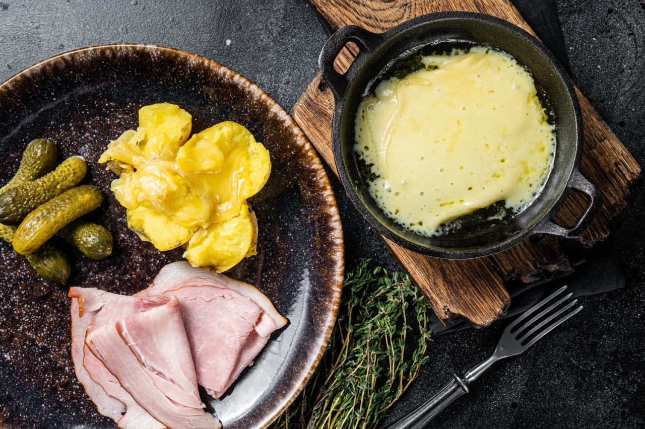 raclette melted cheese with boiled potato ham rustic plate swiss meal black background top view