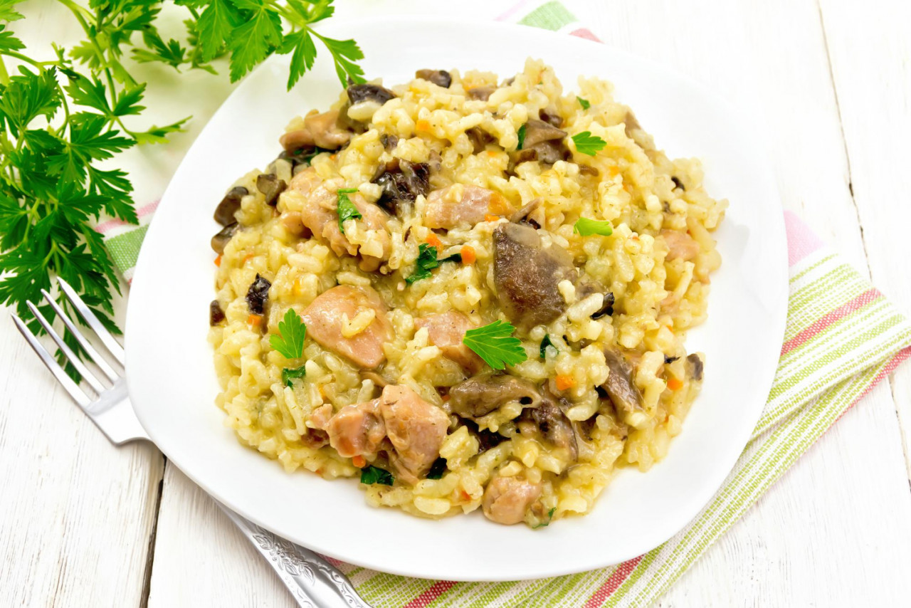 rice risotto with mushrooms chicken meat cheese garlic plate kitchen towel fork parsley wooden board background