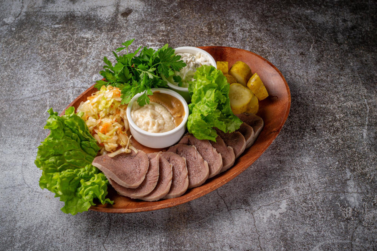 serving dish from restaurant menu sliced beef tongue with pickles cabbage sauces herbs plate against gray stone table delicious appetizer