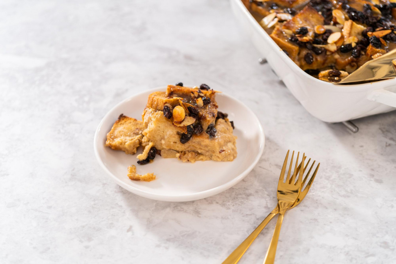 serving freshly baked bread pudding with raising almond slivers white casserole dish
