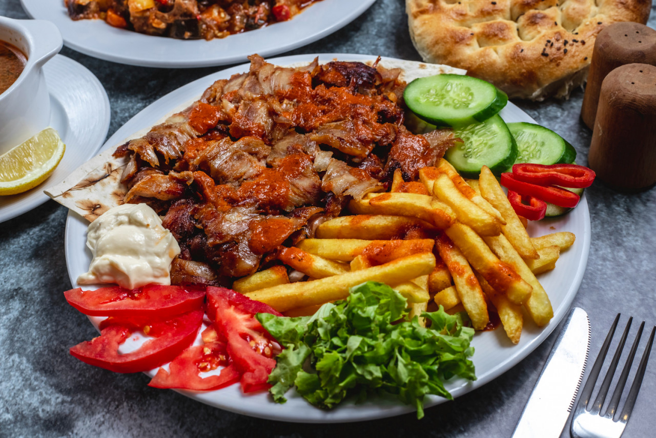 side view doner plate with french fries tomato fresh cucumber yogurt bread table