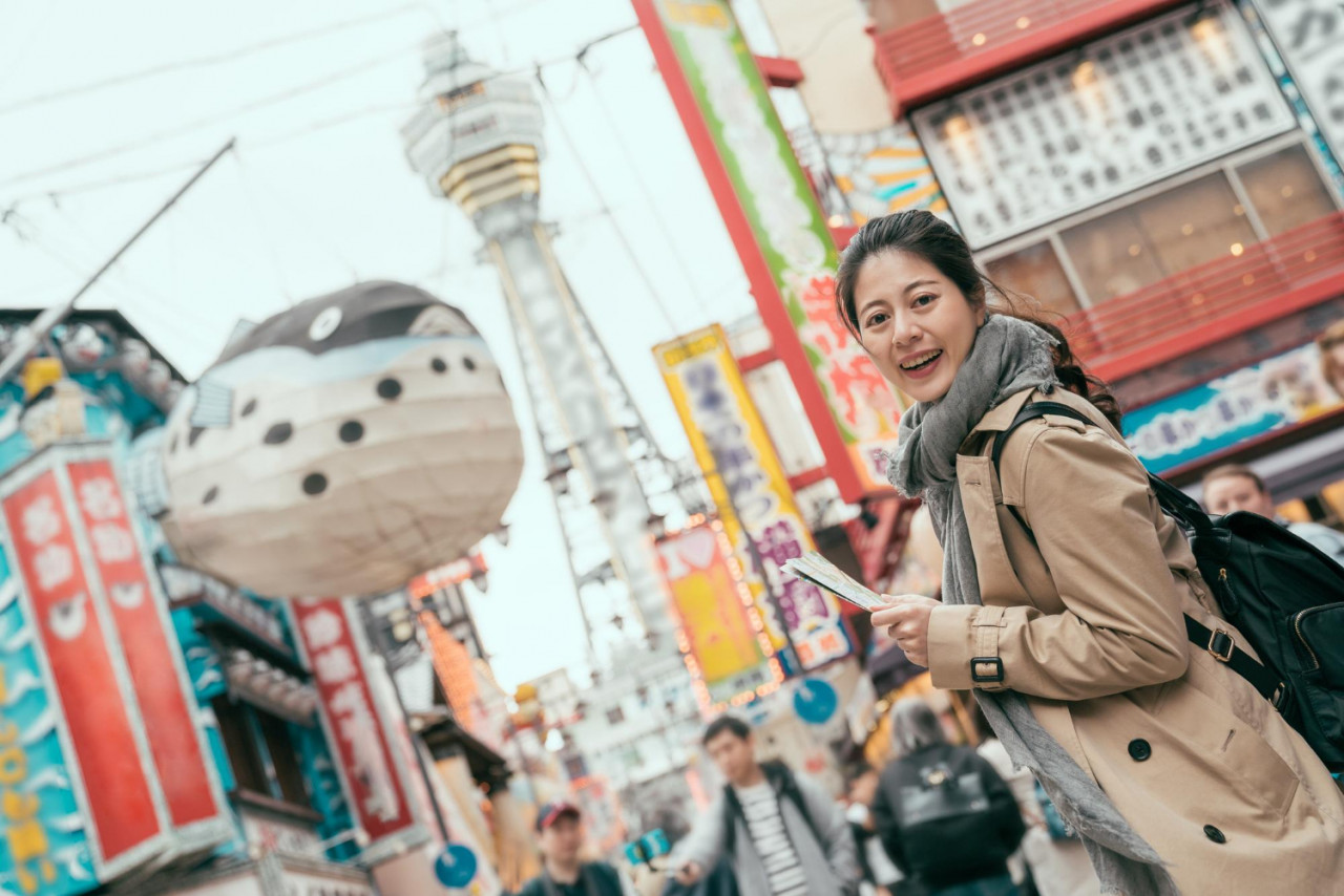 side view young girl standing dotonbori shinsaibashi puffer fish balloon tsutenkaku background female asian chinese tourist face camera smiling charming while holding map bag