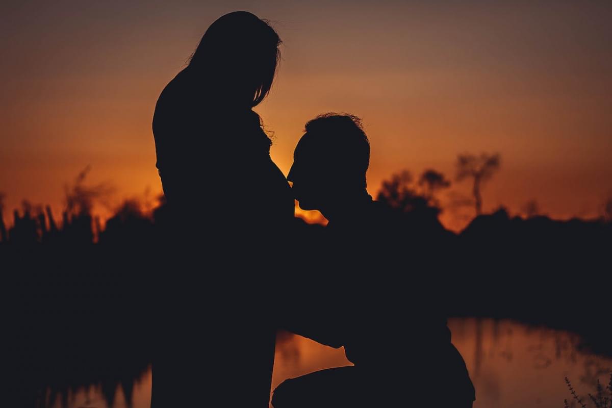 silhouette photo of man kissing his wife pregnant stomach 1