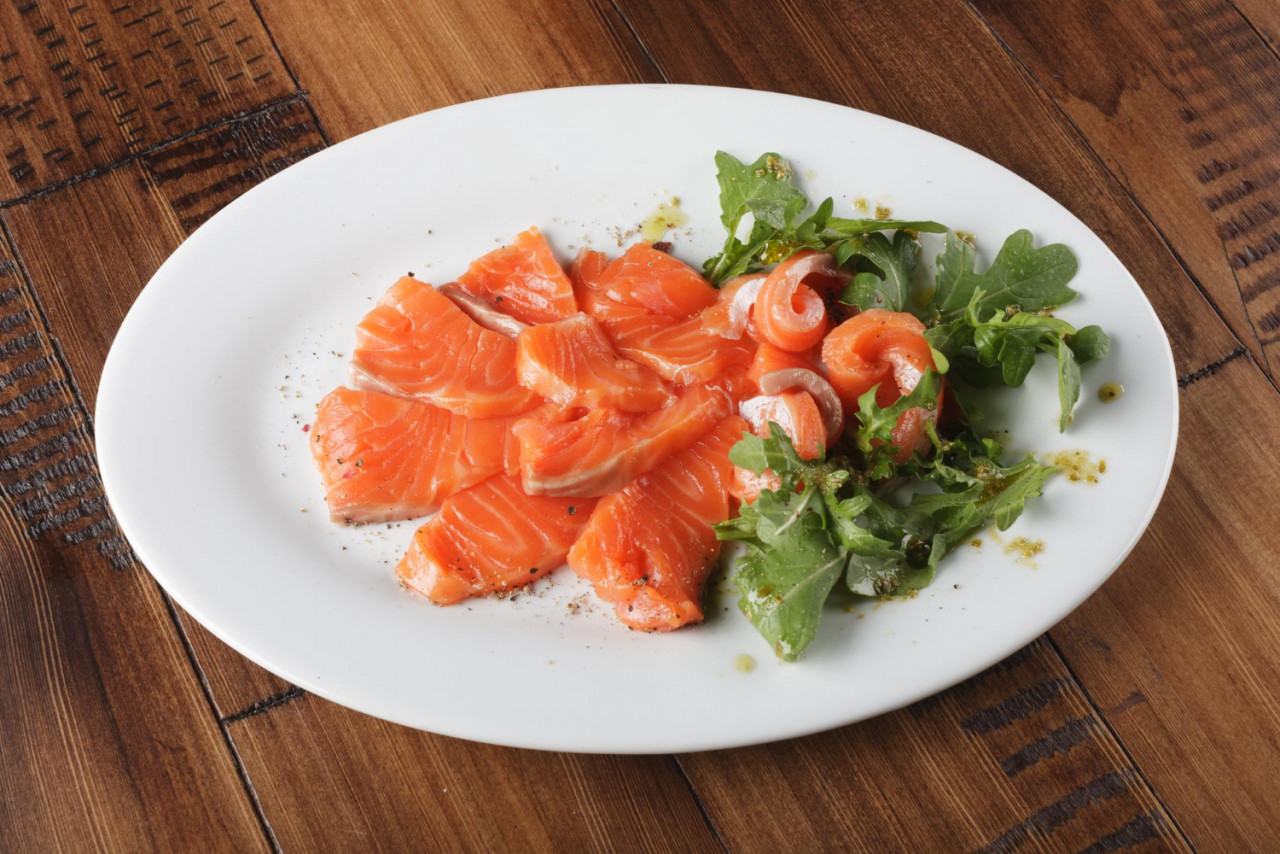 smoked trout with greens white plate wooden background