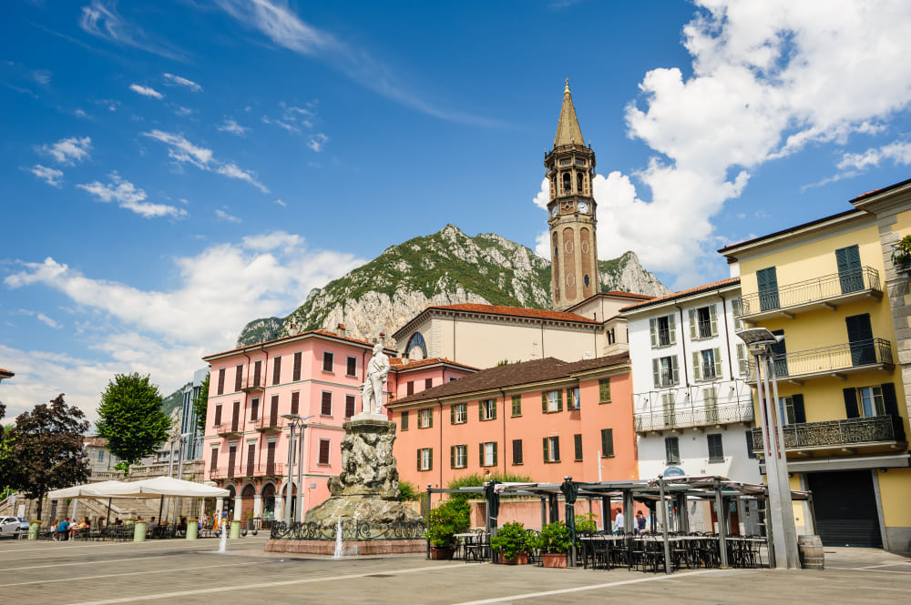 strade centrali della citta di lecco con bar e campanile il monumento di mario cermenati in primo piano