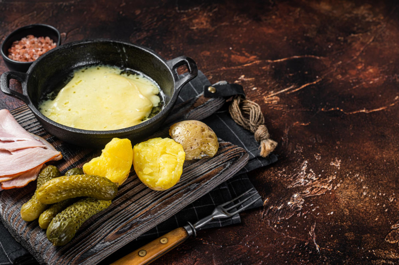 swiss raclette melted cheese with boiled potato ham wooden board dark background top view copy space