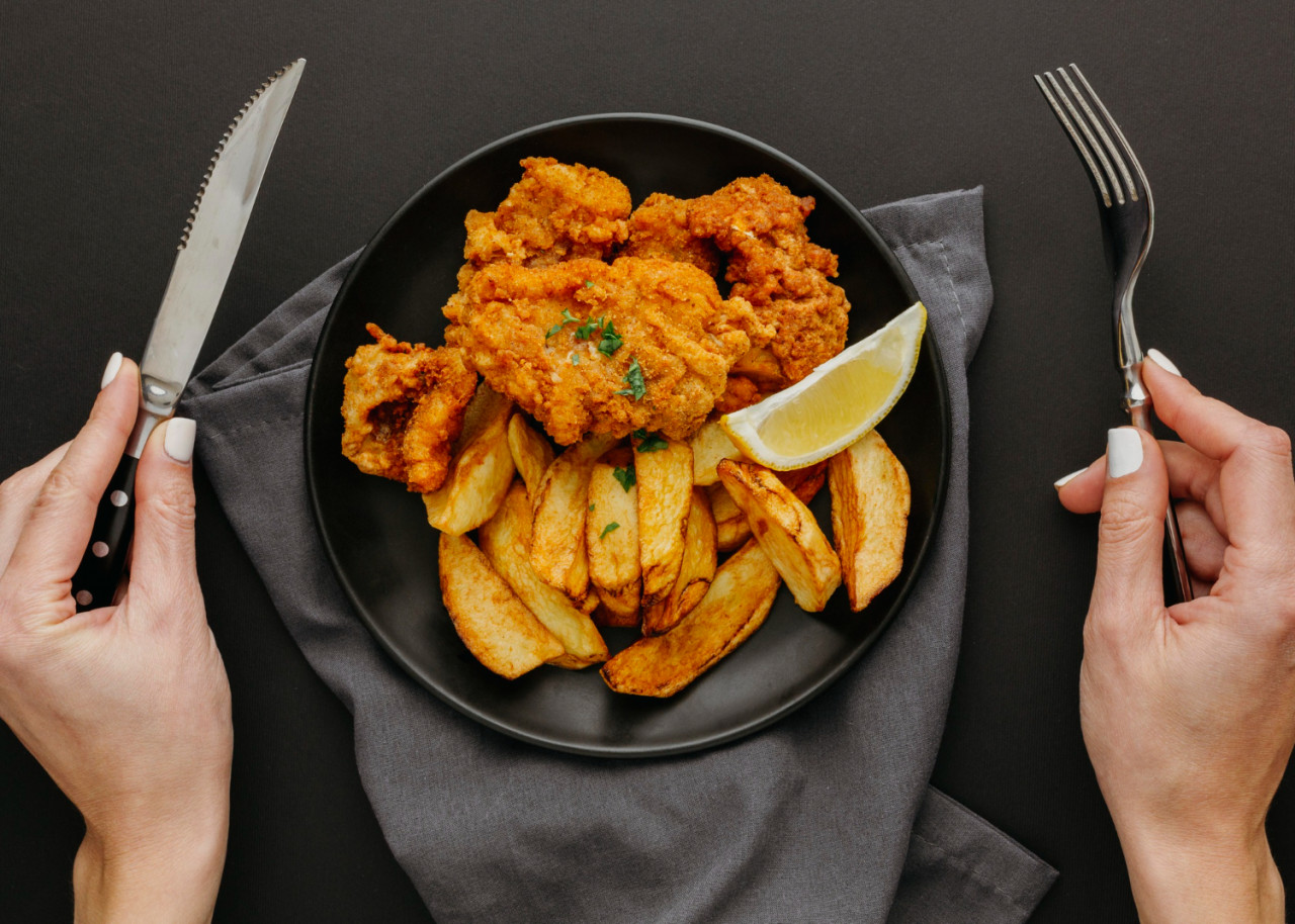 top view of fish and chips on plate with woman holding cutlery