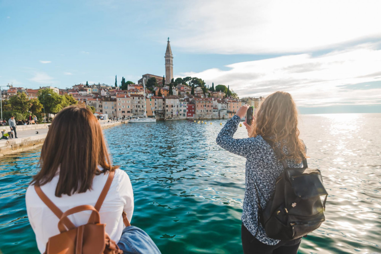 woman traveler looking rovinj city from harbour taking picture phone