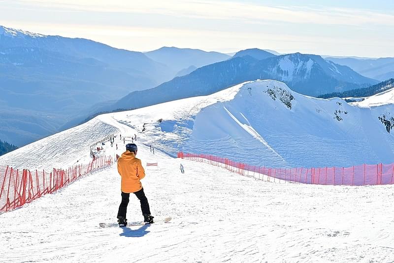 young snowboarder on the slope of a ski resort with a panoramic view of the mountains at sunset