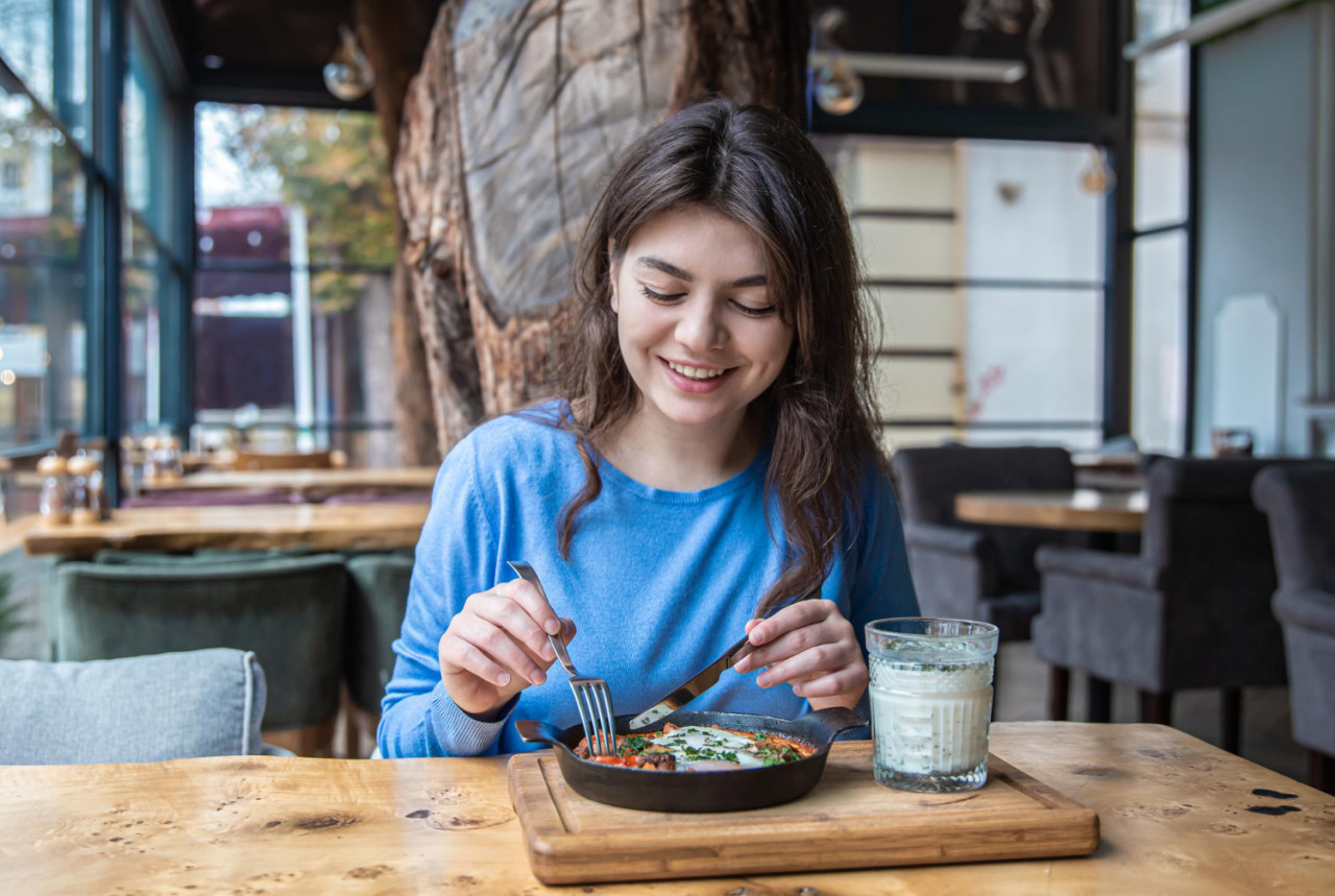 young woman cafe dines traditional shakshuka ayran