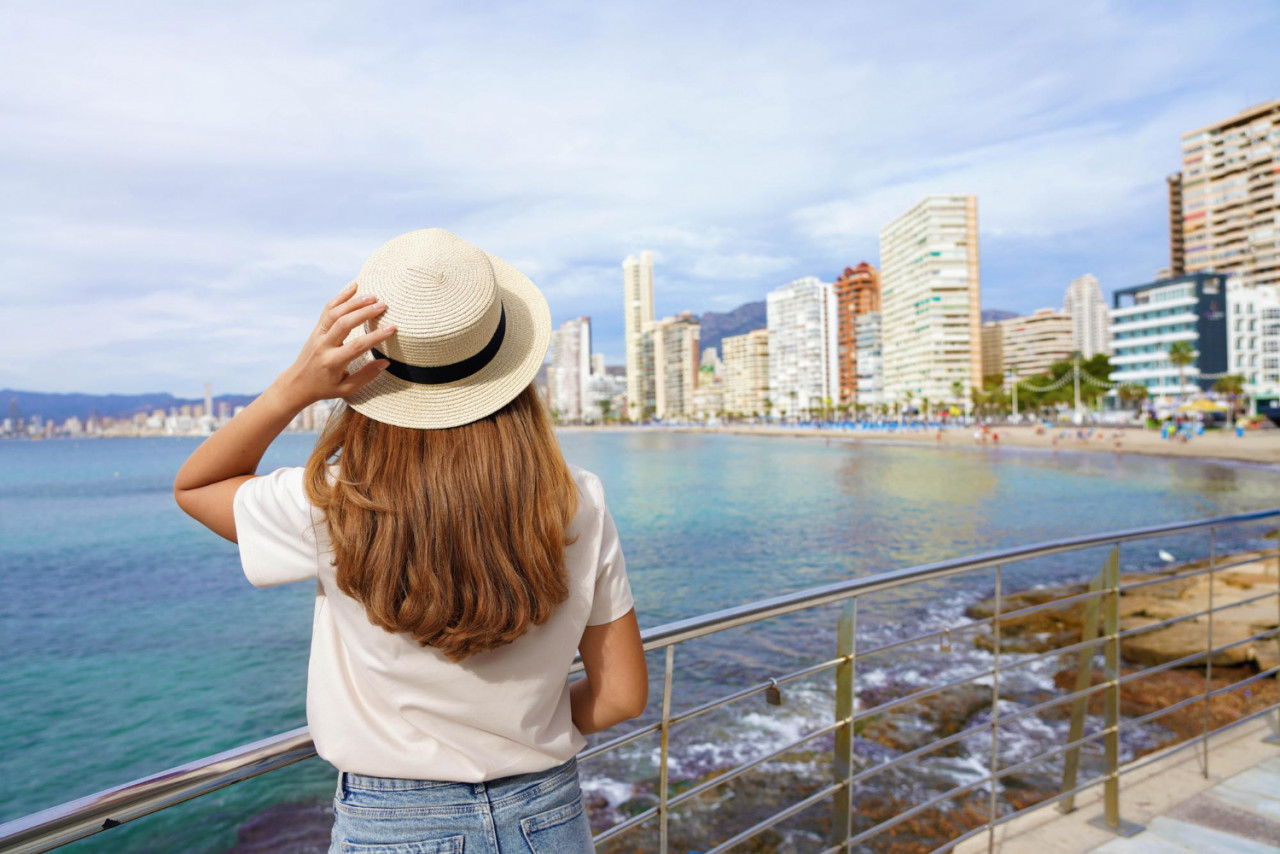 young woman holds hat promenade front skyline from benidorm downtown spain